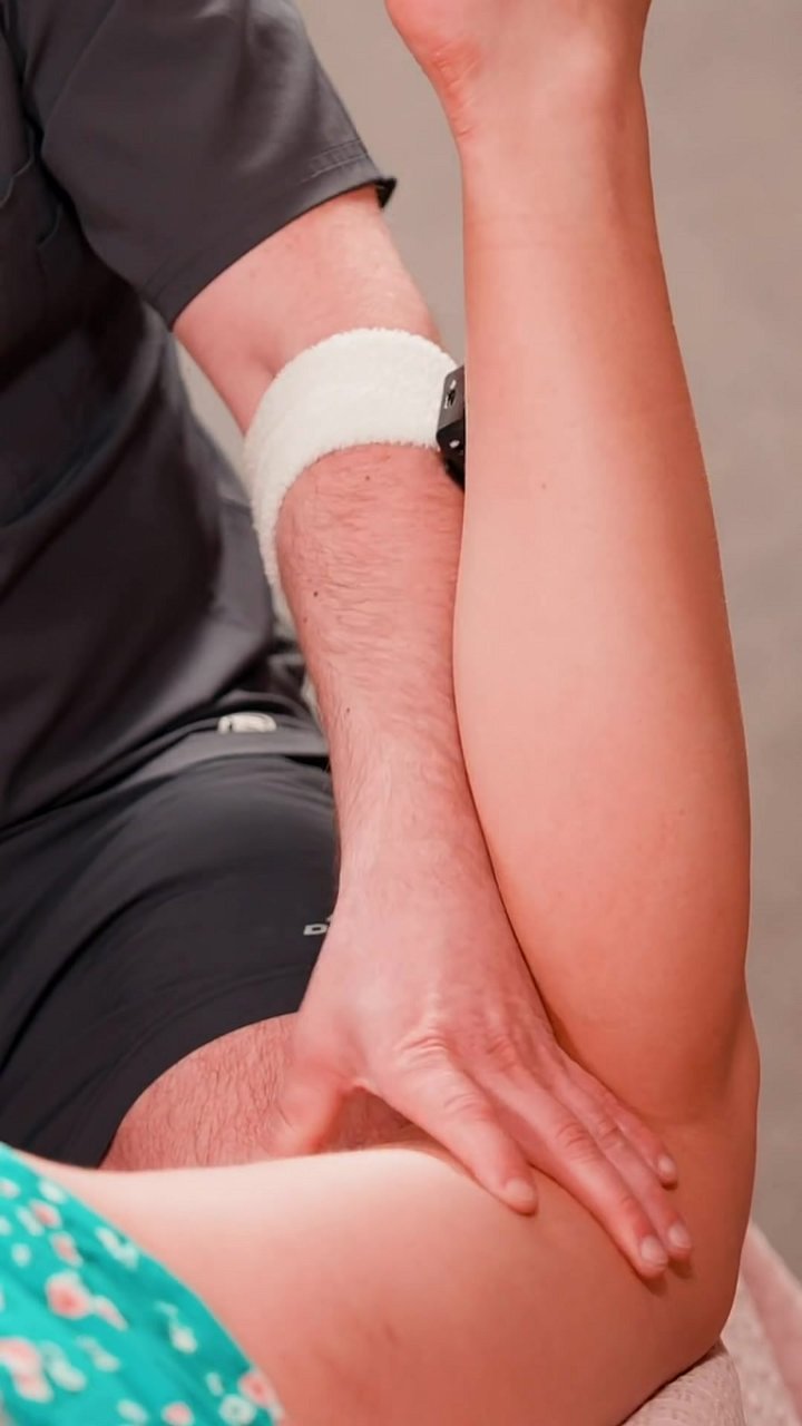 Why does deep tissue work on the quadriceps often elicit this response? Here, the practitioner is applying sustained forearm pressure to the client's thigh and calf. This myofascial technique targets deep fascial adhesions to restore mobility. The grimace